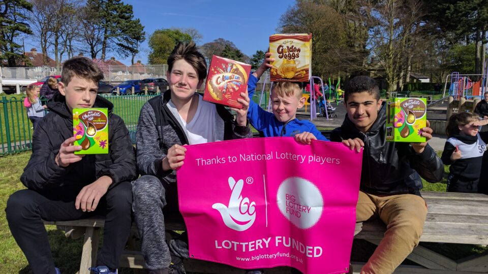 Young People Holding Easter Eggs and Lottery Funded Banner